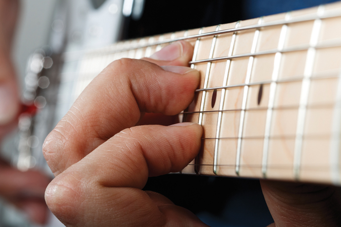 Hands of man playing electric guitar with red pick closeup