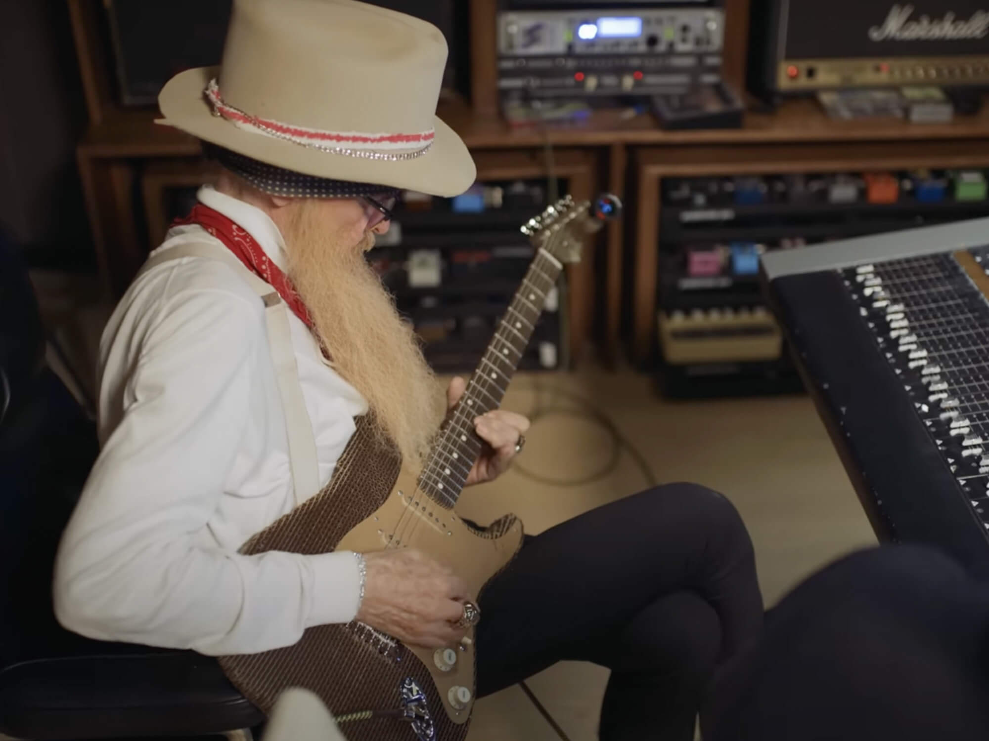 Billy Gibbons playing the Stratocaster, it is of a brown colour with a gold scratch plate. The body looks similar to corrugated cardboard.