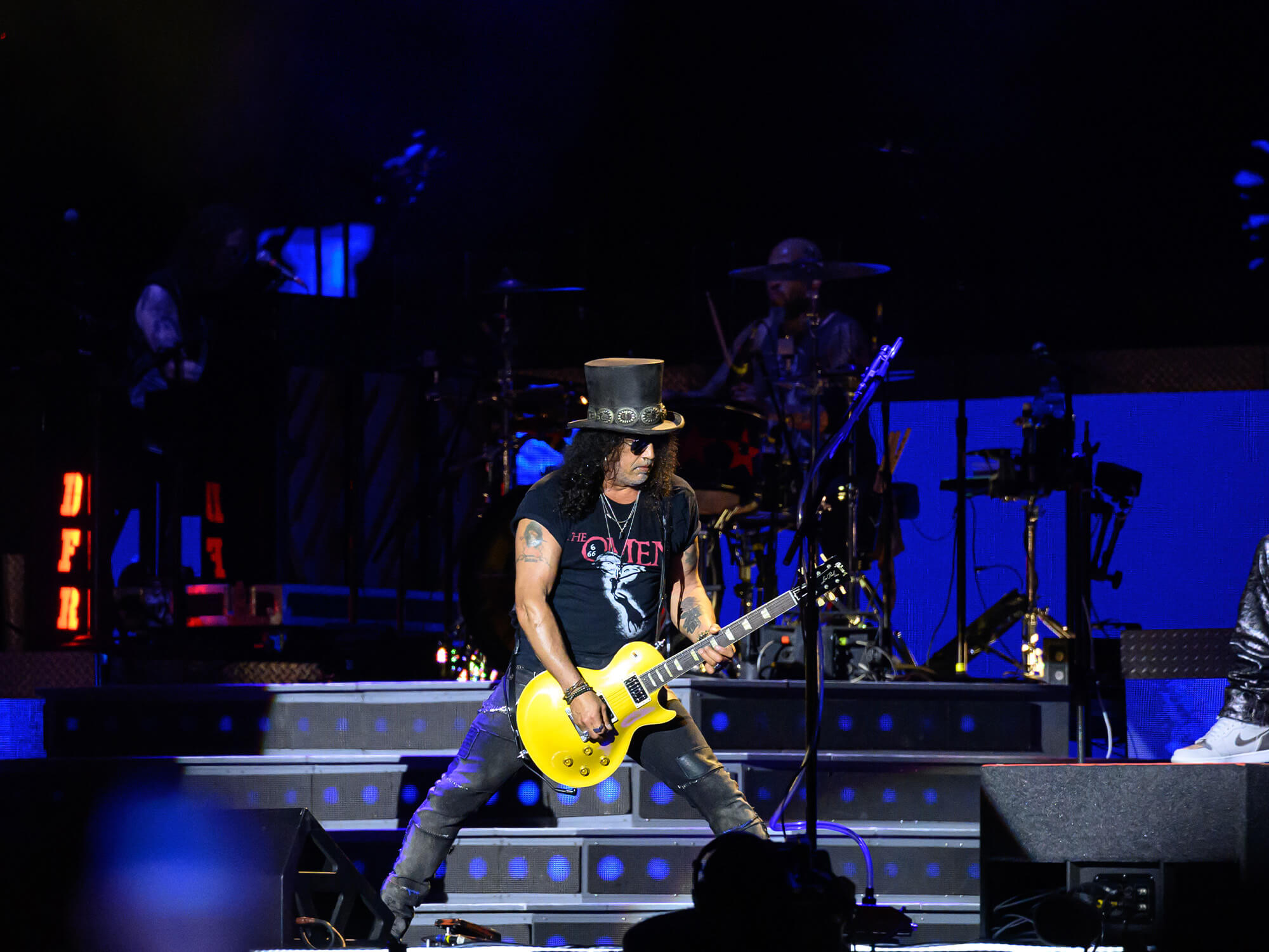 Slash on stage, he is wearing his famous top hat and stands with his legs spread slightly apart as he plays a Gibson Les Paul