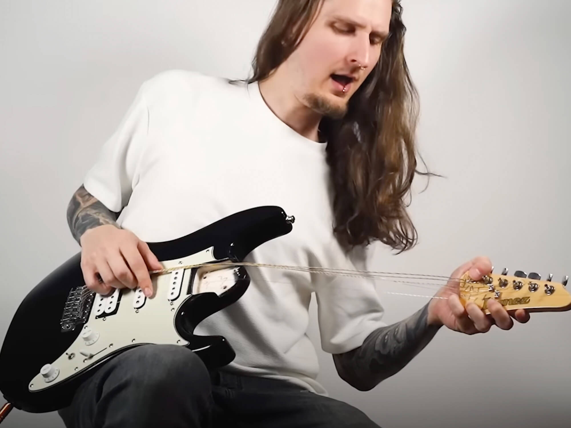 Screencap from Bernth's video showing him playing the black Strat model. He's holding the headstock to pull the strings.
