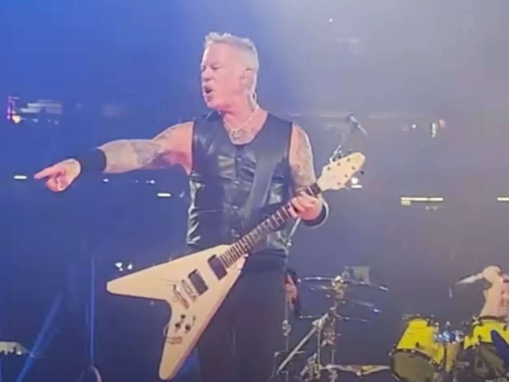 James Hetfield playing his white Gibson Flying V. He's pointing into the crowd with a stern expression.
