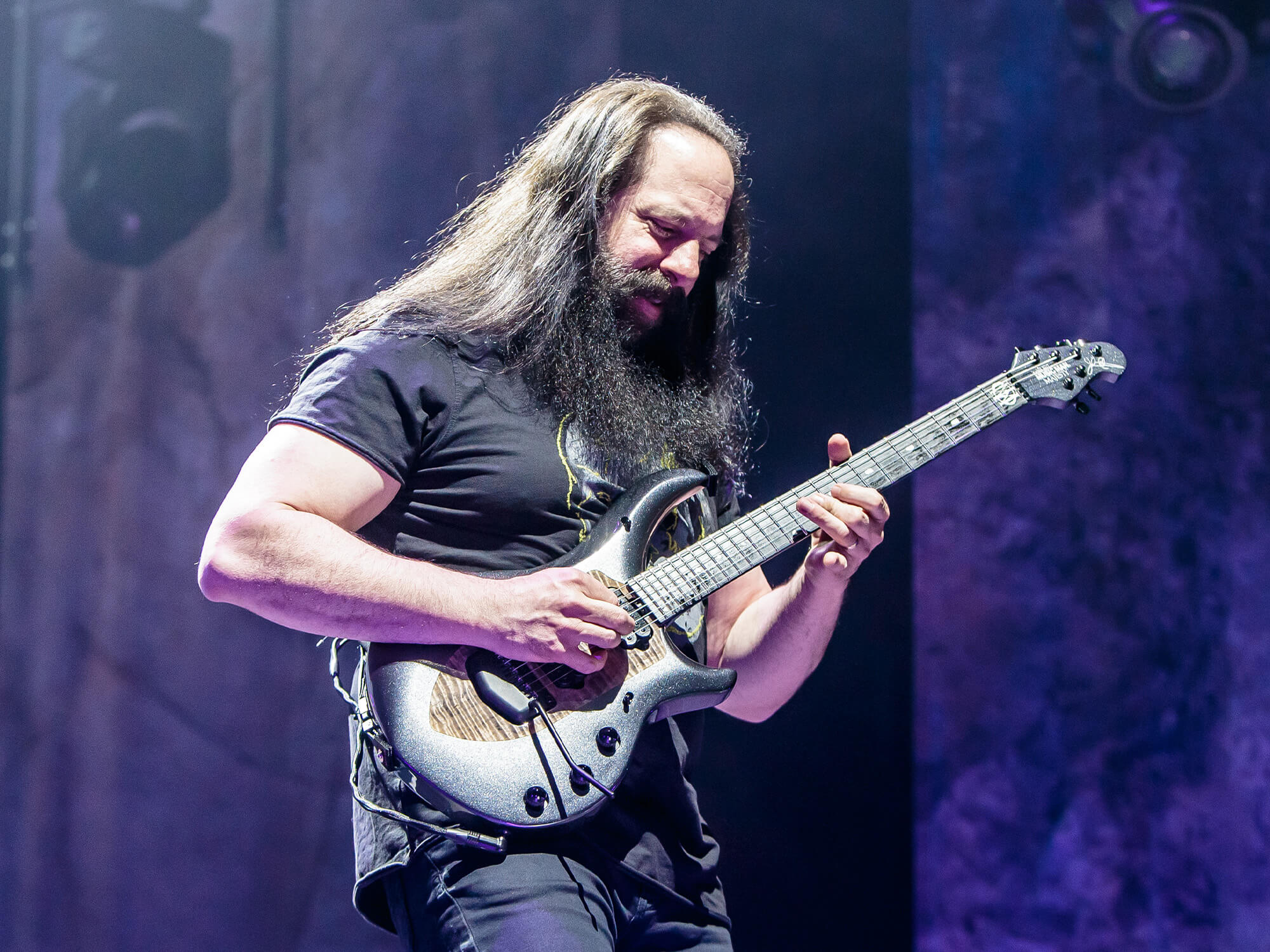 John Petrucci on stage playing an Ernie Ball Music Man electric guitar