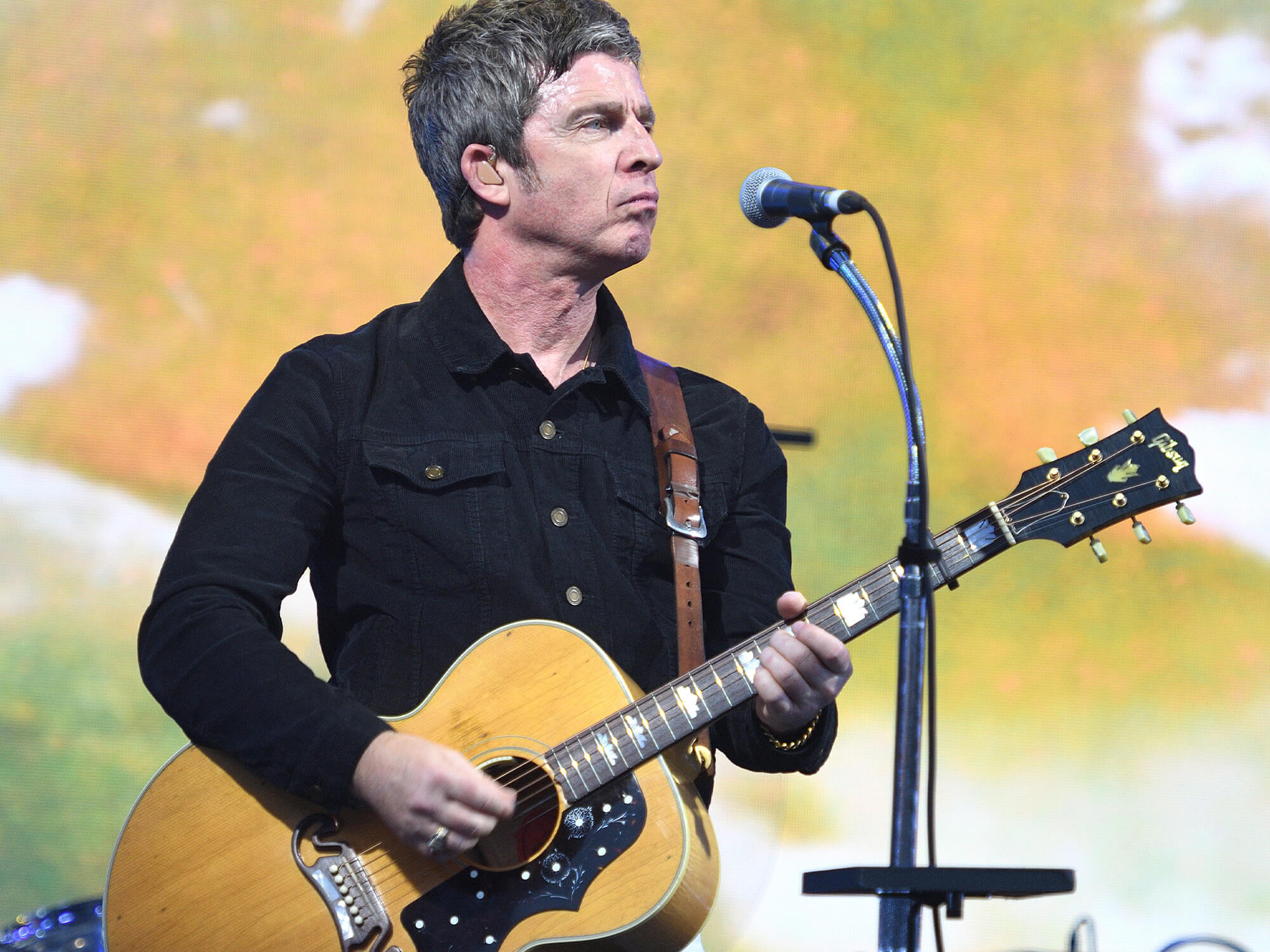 Noel Gallagher on stage playing a Gibson acoustic