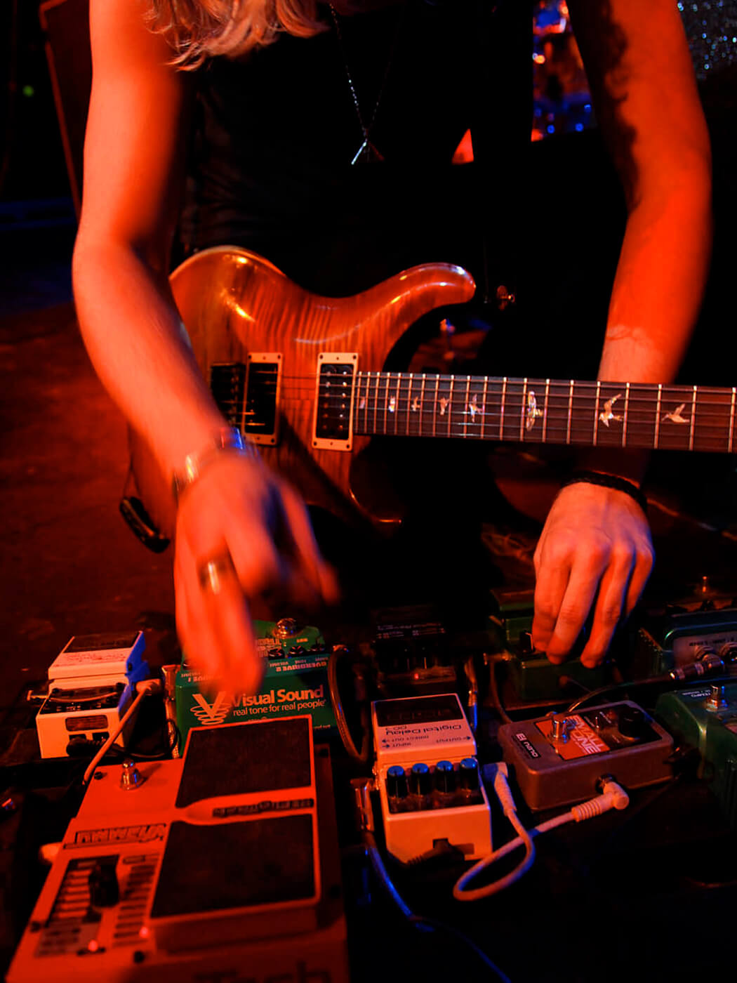 A guitarist altering guitar effects pedals onstage