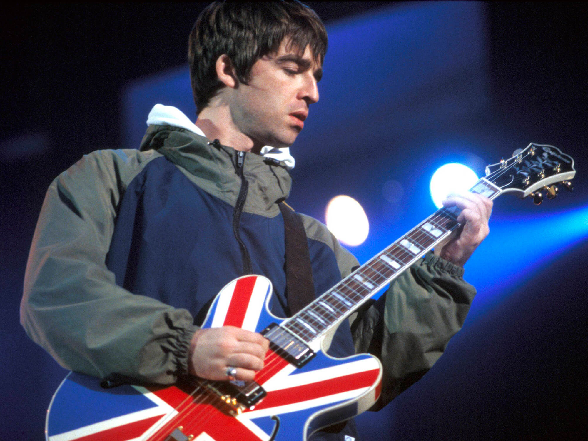 Noel Gallagher playing an Epiphone Sheraton Union Jack guitar onstage in 1996 by Patrick Ford/Redferns via Getty Images