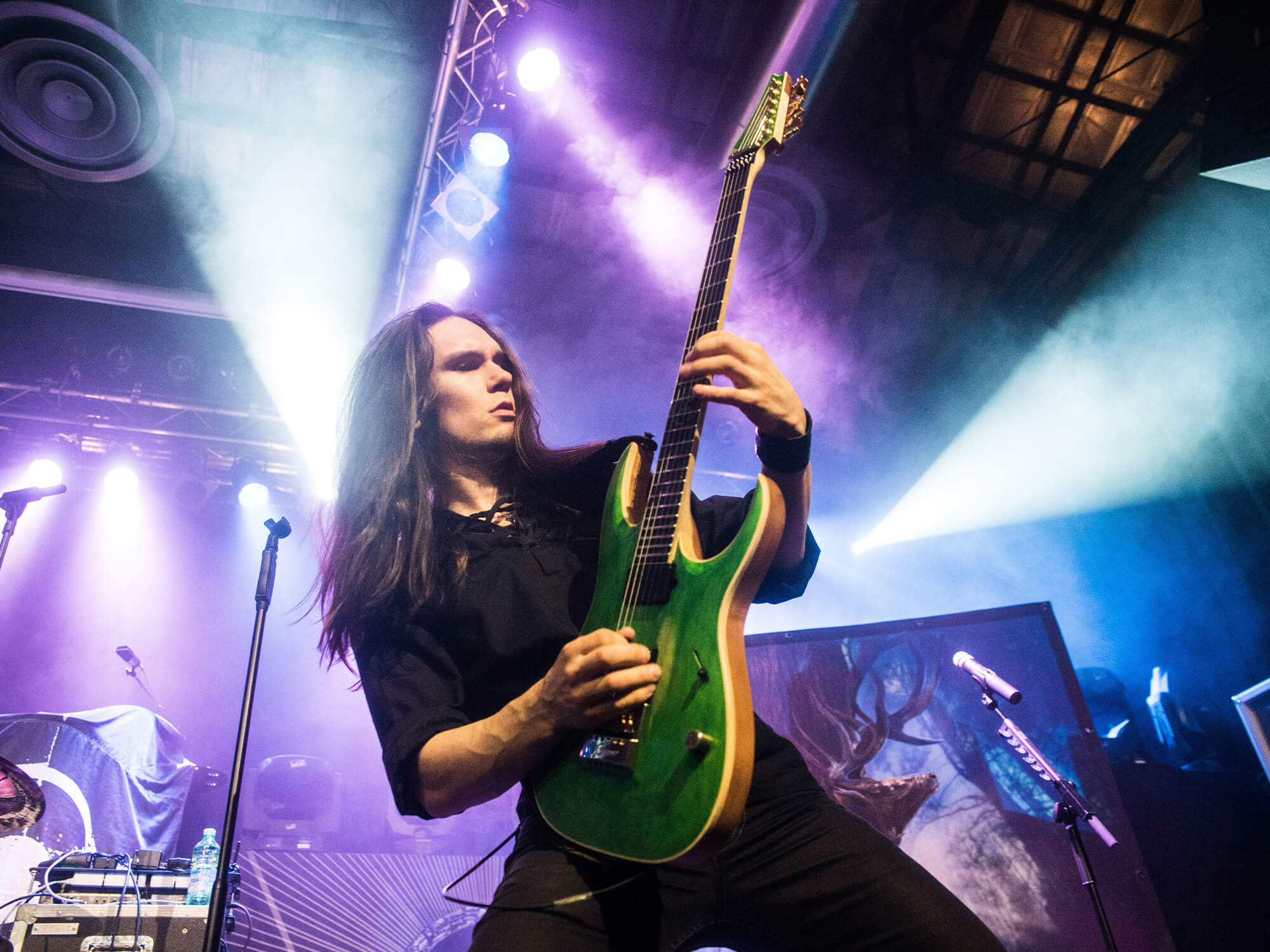 Teemu Mäntysaari on stage in 2018. He's playing a bright green electric guitar which he is holding upright.
