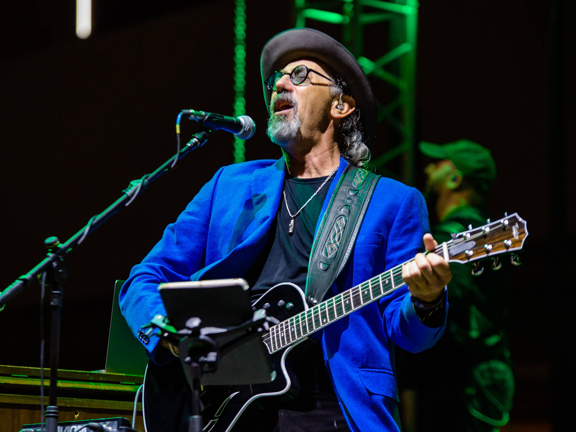 Jack Sonni on stage in 2019. He's singing and playing an acoustic guitar, and wears a bright blue blazer
