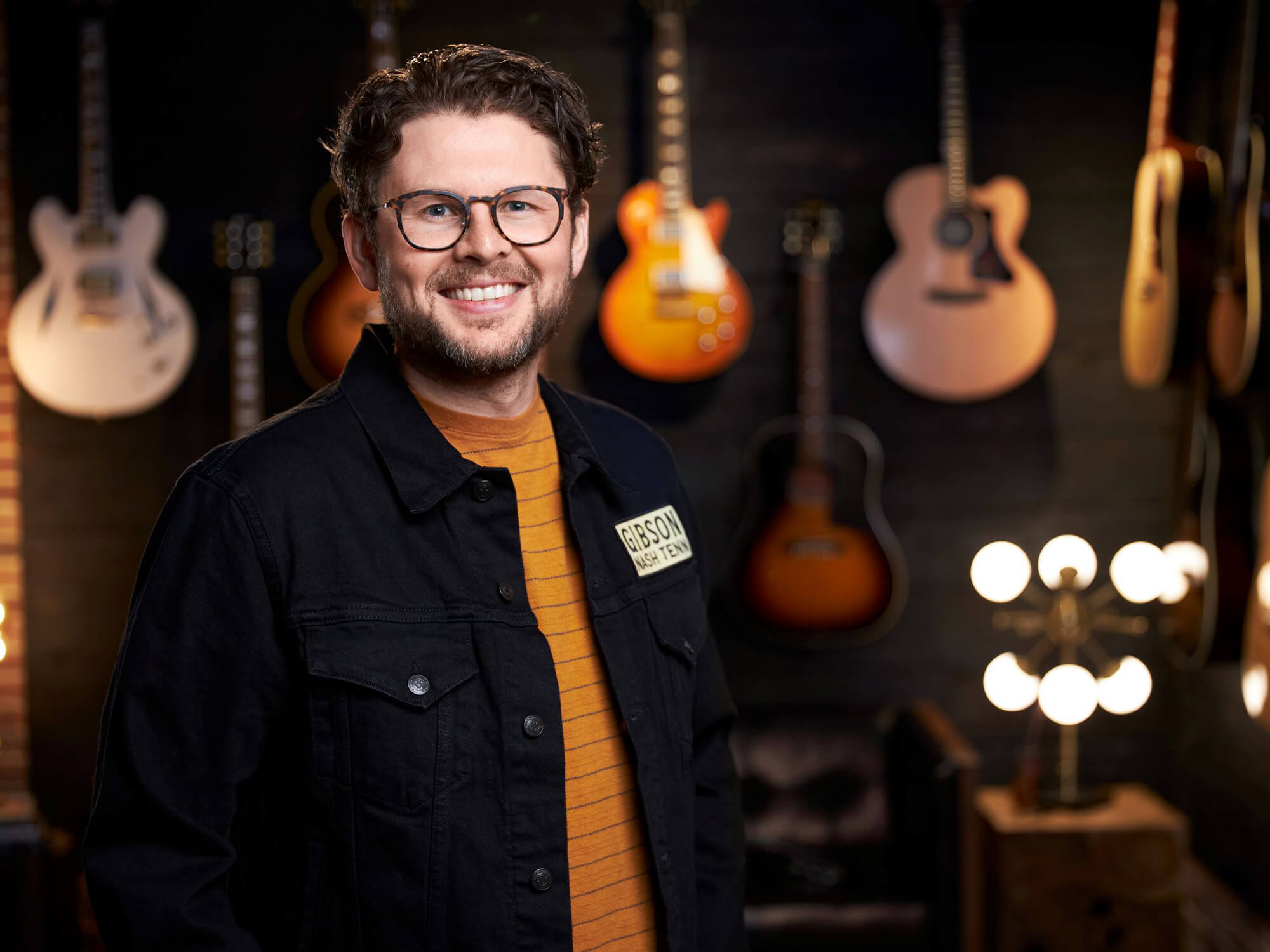 Mat Koehler smiling in front of a wall of Gibson guitars.