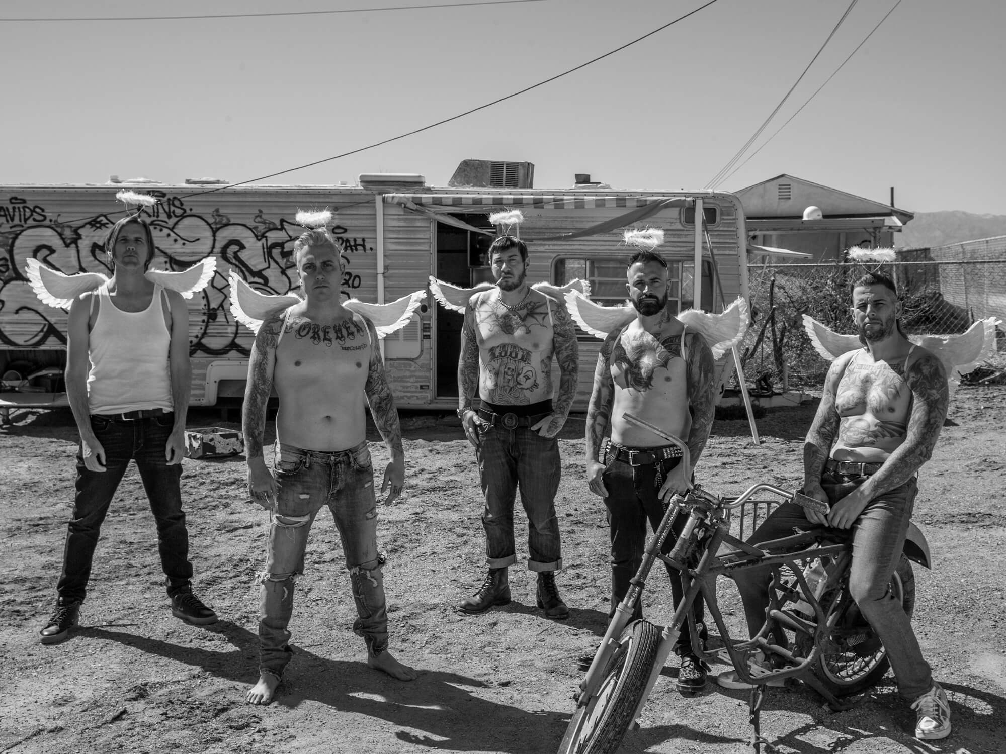Black and white photo of the band wearing angel wings and halos outside of an old trailer