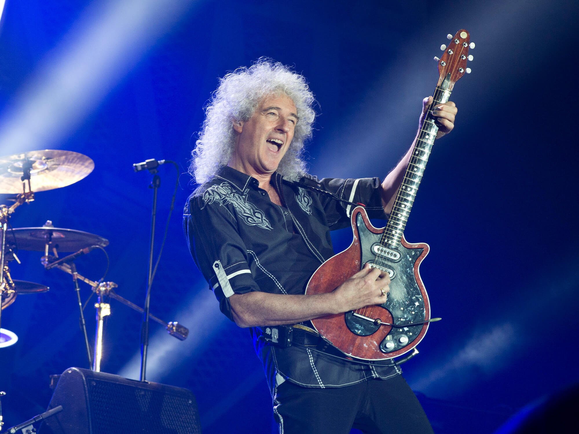 Brian May holding his Red Special up right, with his mouth open in a joyful expression