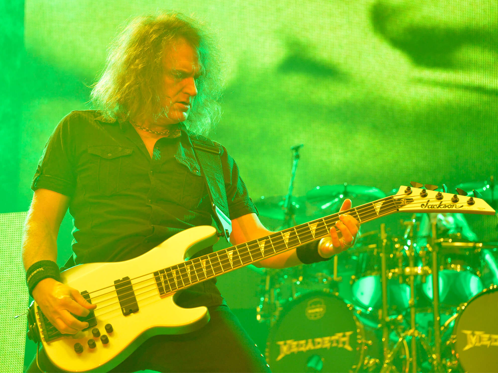 David Ellefson on stage in 2015. He plays a Jackson bass guitar and stands under green lighting.