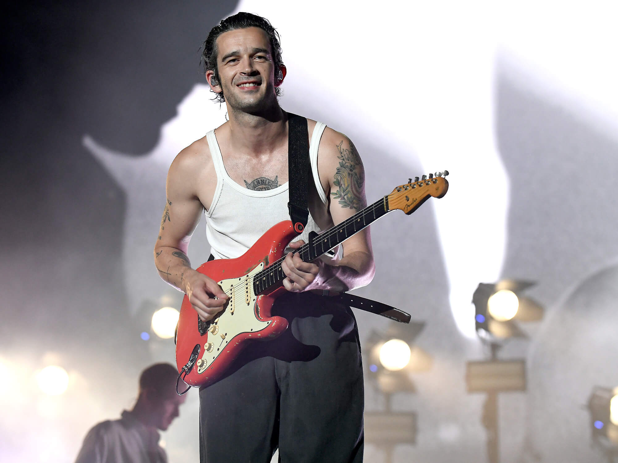 Matty Healy playing a red Strat and smiling at the crowd