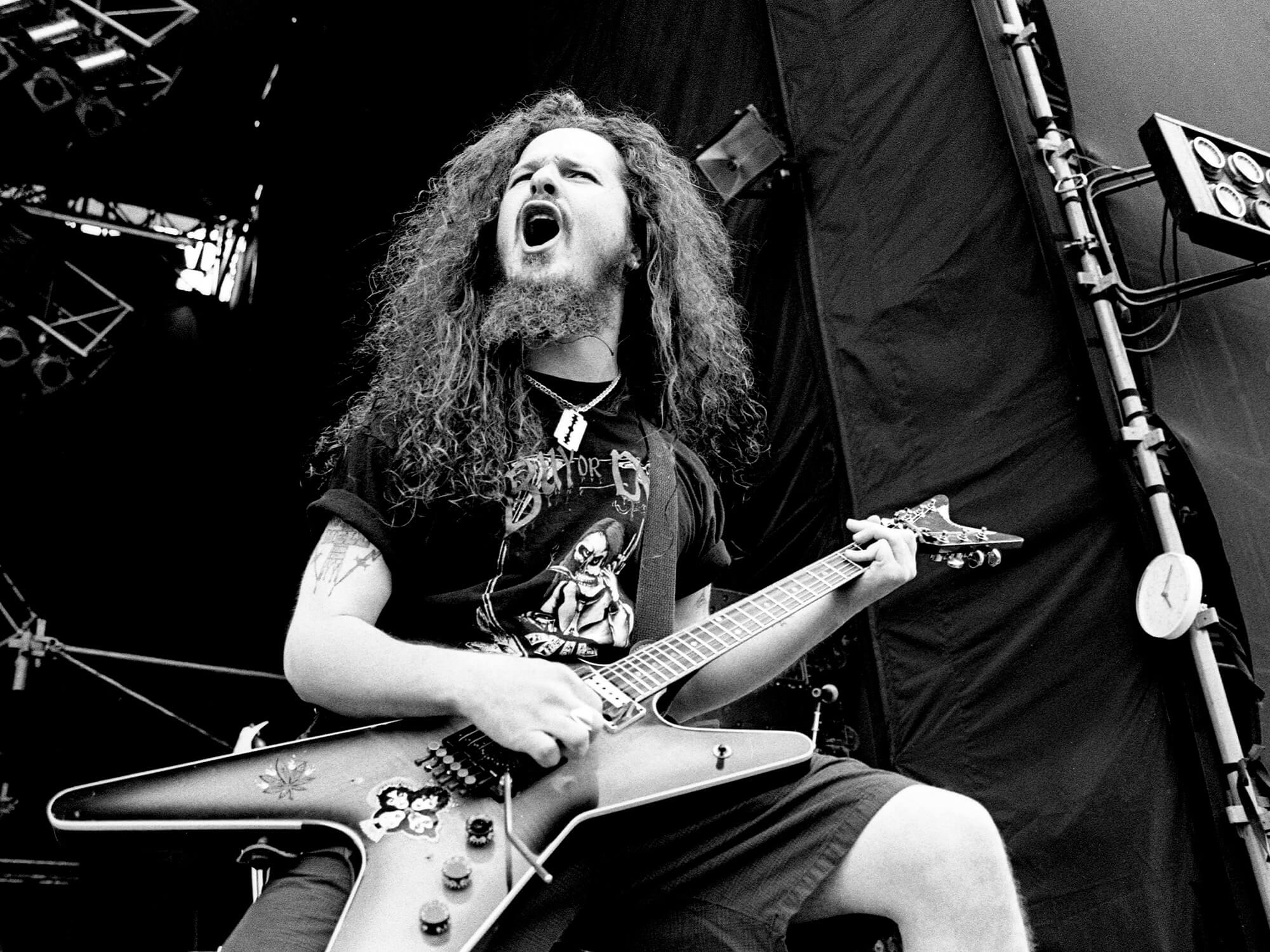 Dimebag Darrell of Pantera on stage in 1994. Photo is black and white, and shows him playing guitar and calling out into the crowd.
