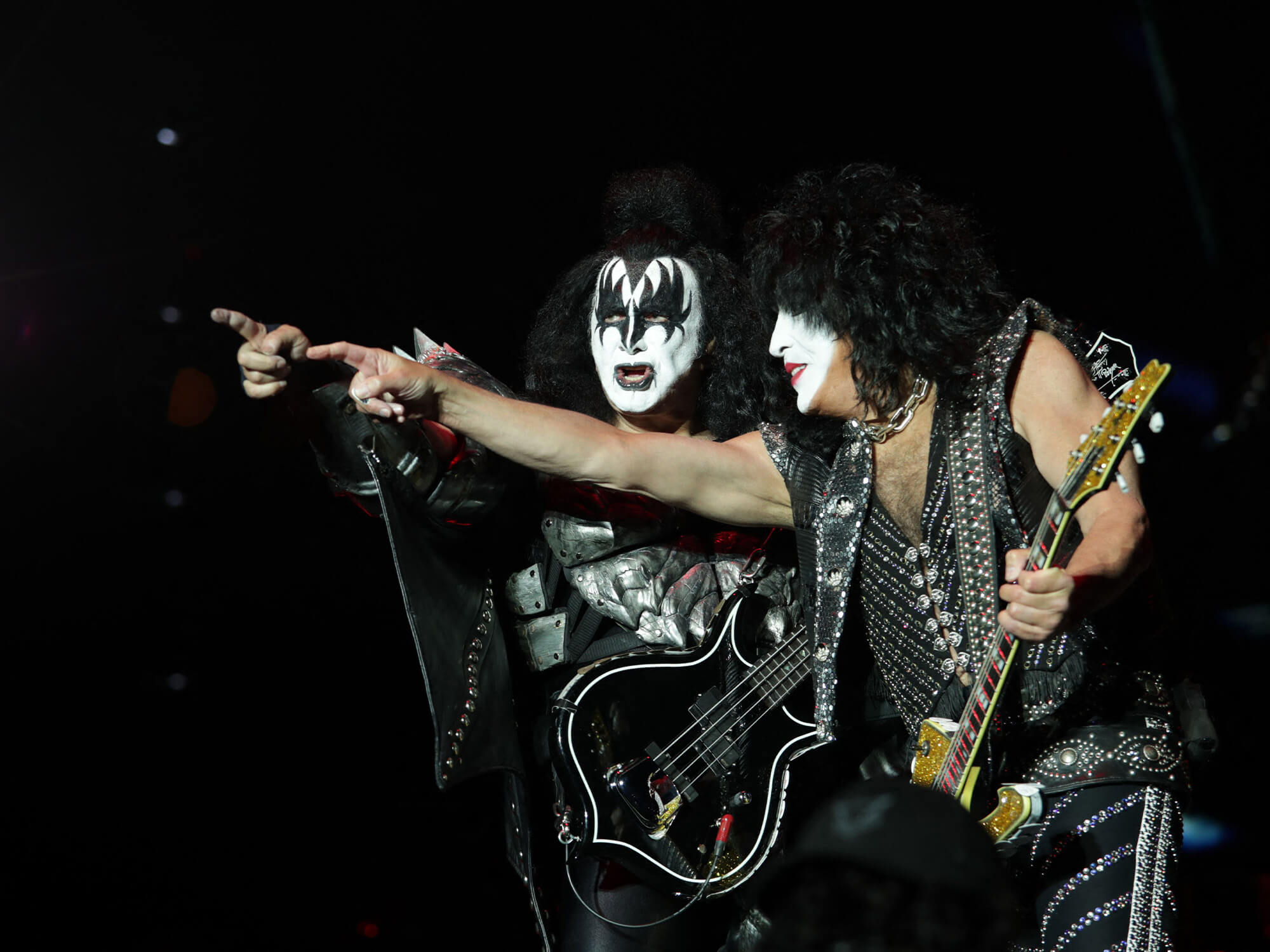Gene Simmons and Paul Stanley on stage with their guitars in hand. They are wearing their signature stage makeup and are both pointing out into the crowd.