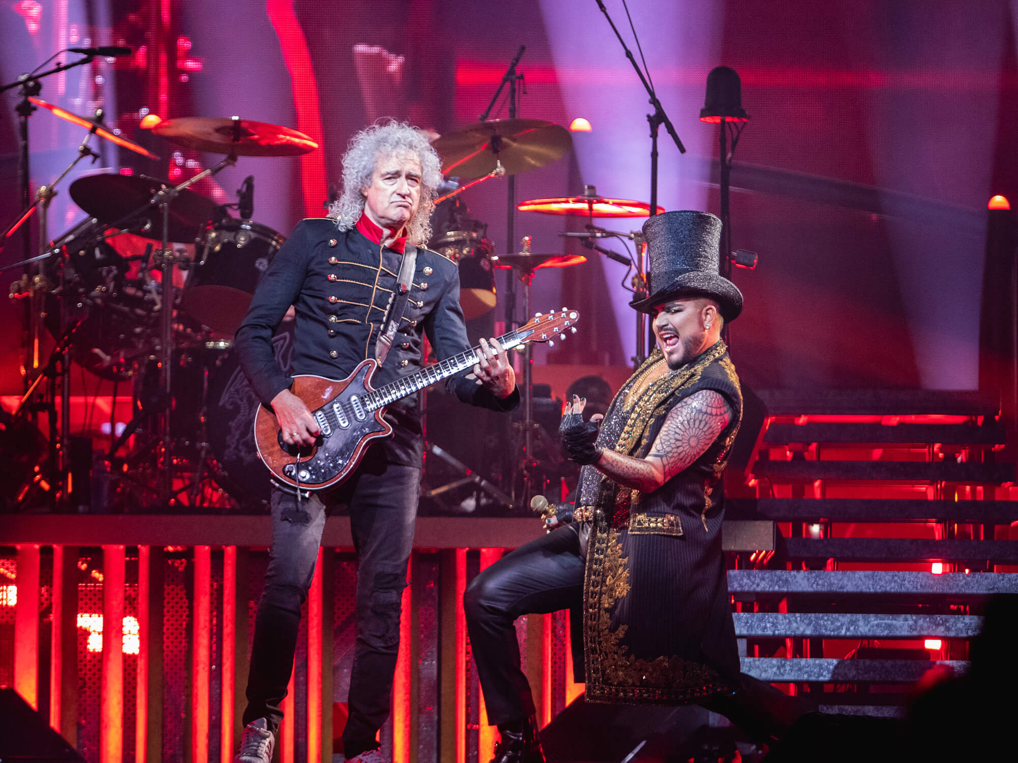 Brian May with his Red Special. Adam Lambert is down on one knee next to him wearing a top hat and playing air guitar.