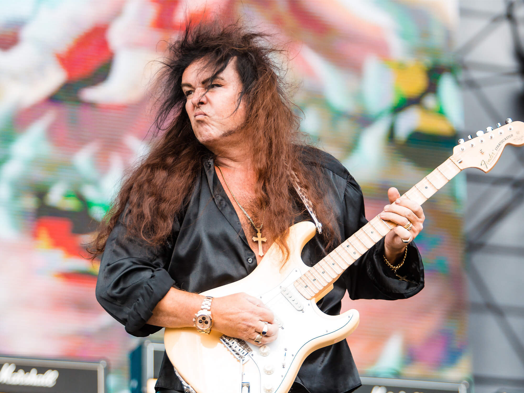 Yngwie Malmsteen on stage. He plays a white Strat and is pouting as he plays.