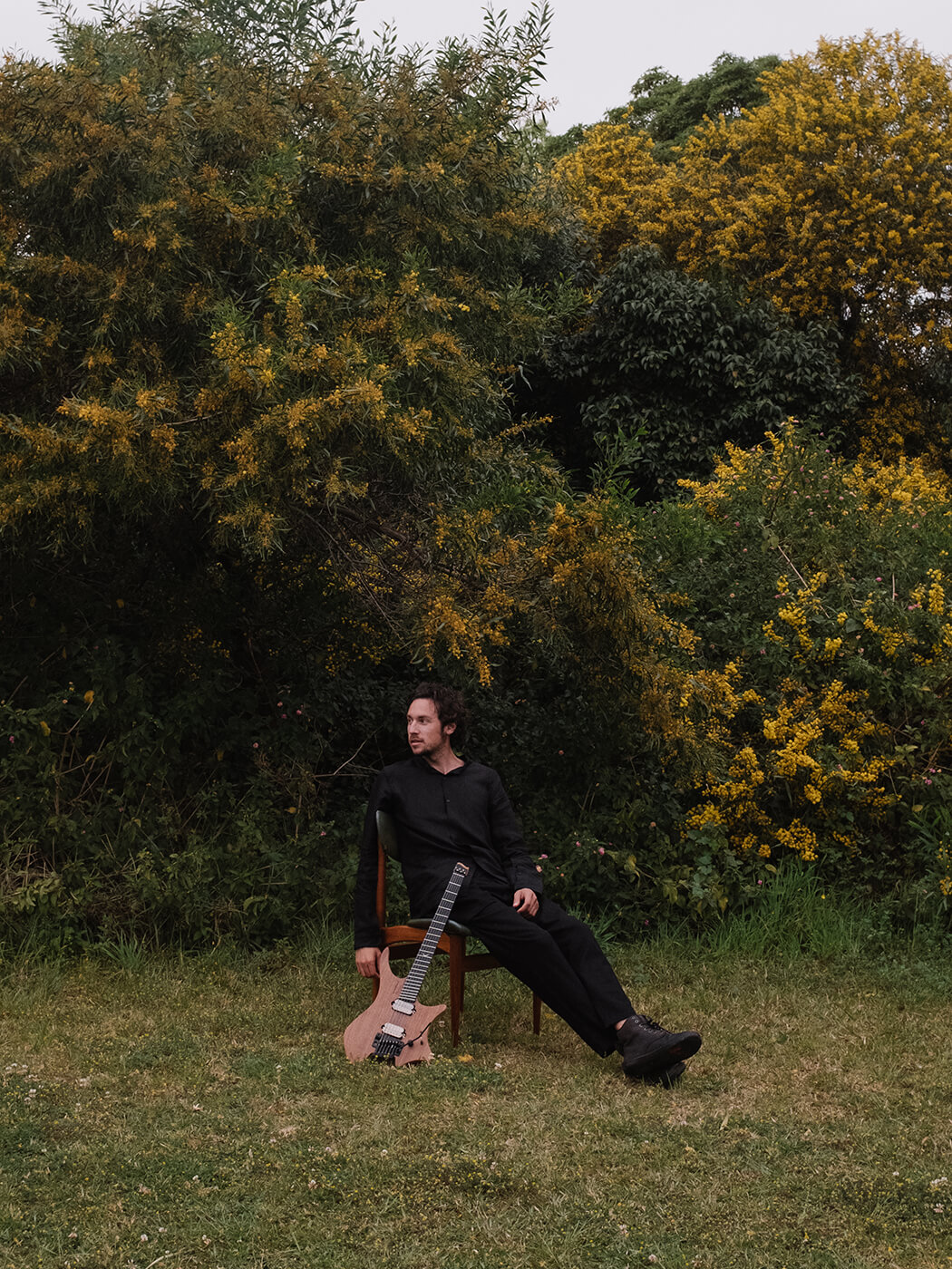 Plini seated on a chair with his Strandberg guitar in a field with trees, photo by Chad Dao