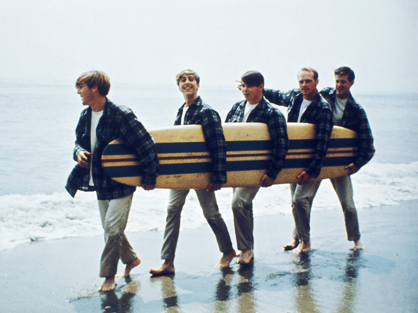 The Beach Boys on a beach holding a surfboard. Left to right: Dennis Wilson, David Marks, Mike Love, Carl Wilson, Brian Wilson. Photo by Michael Ochs Archives/Getty Images