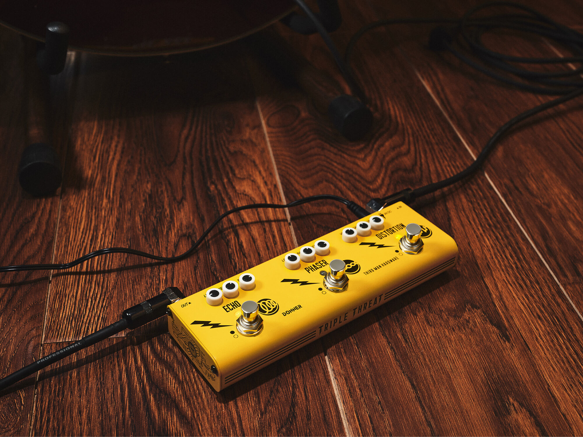 Donner x Third Man Hardware's Triple Threat. The image shows the limited edition Yellow version. It has three main switches, each with three smaller controls. It is plugged in and sits on a wooden floor.