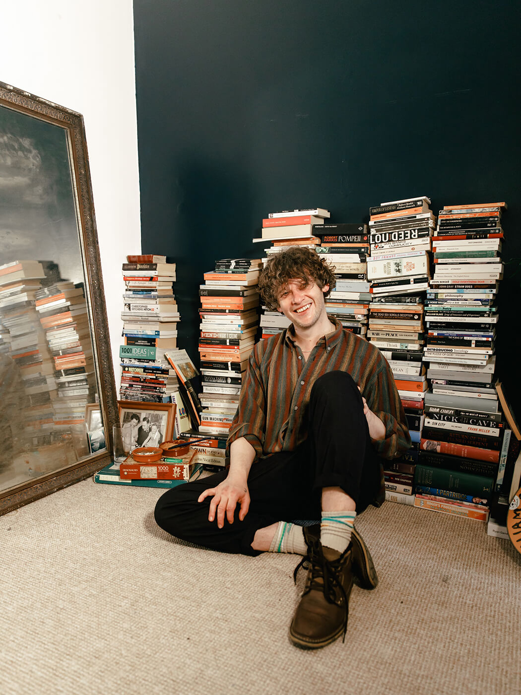 Bill Ryder Jones sitting against piles of books, photo by Marieke Macklon