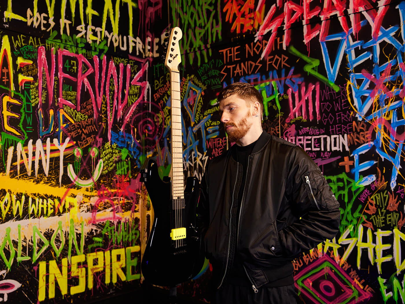 Sean Long with a guitar in a room filled with graffiti
