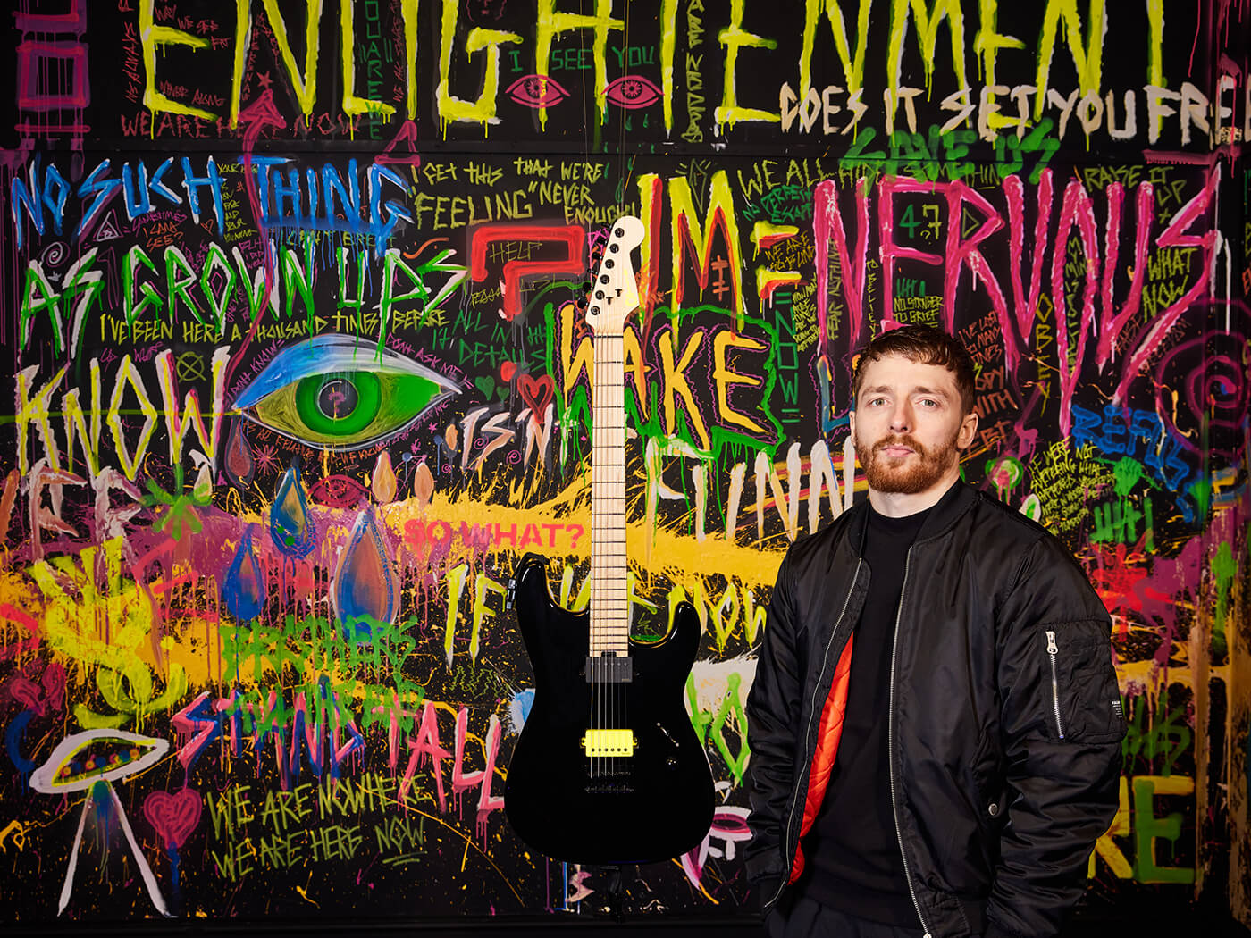 Sean Long with a guitar in a room filled with graffiti