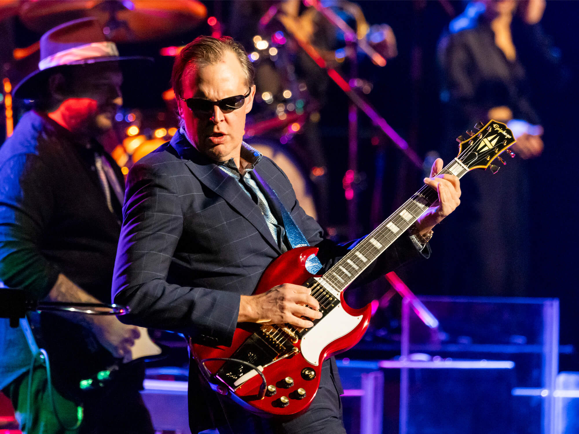 Joe Bonamassa on stage playing an SG. He is wearing a suit and sunglasses.