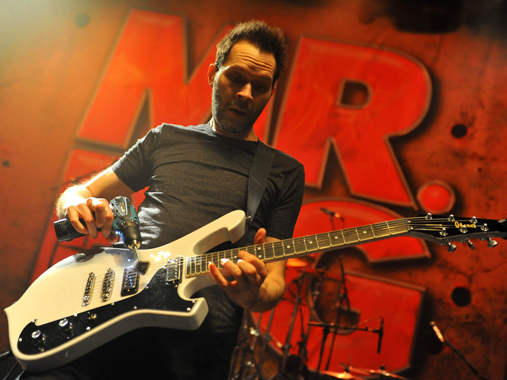 Paul Gilbert playing guitar with a small drill on stage