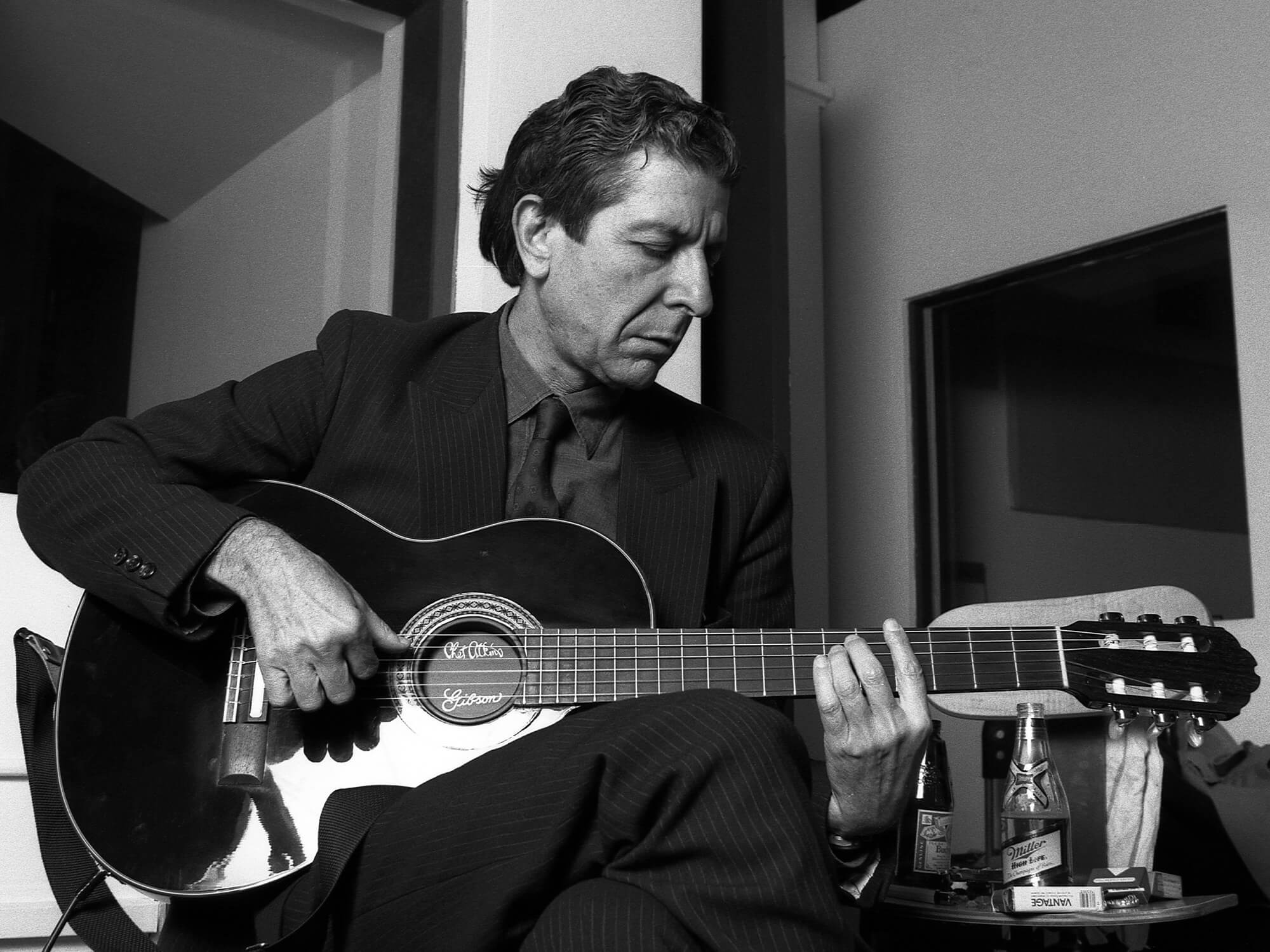 Black and white photo of Leonard Cohen playing acoustic guitar