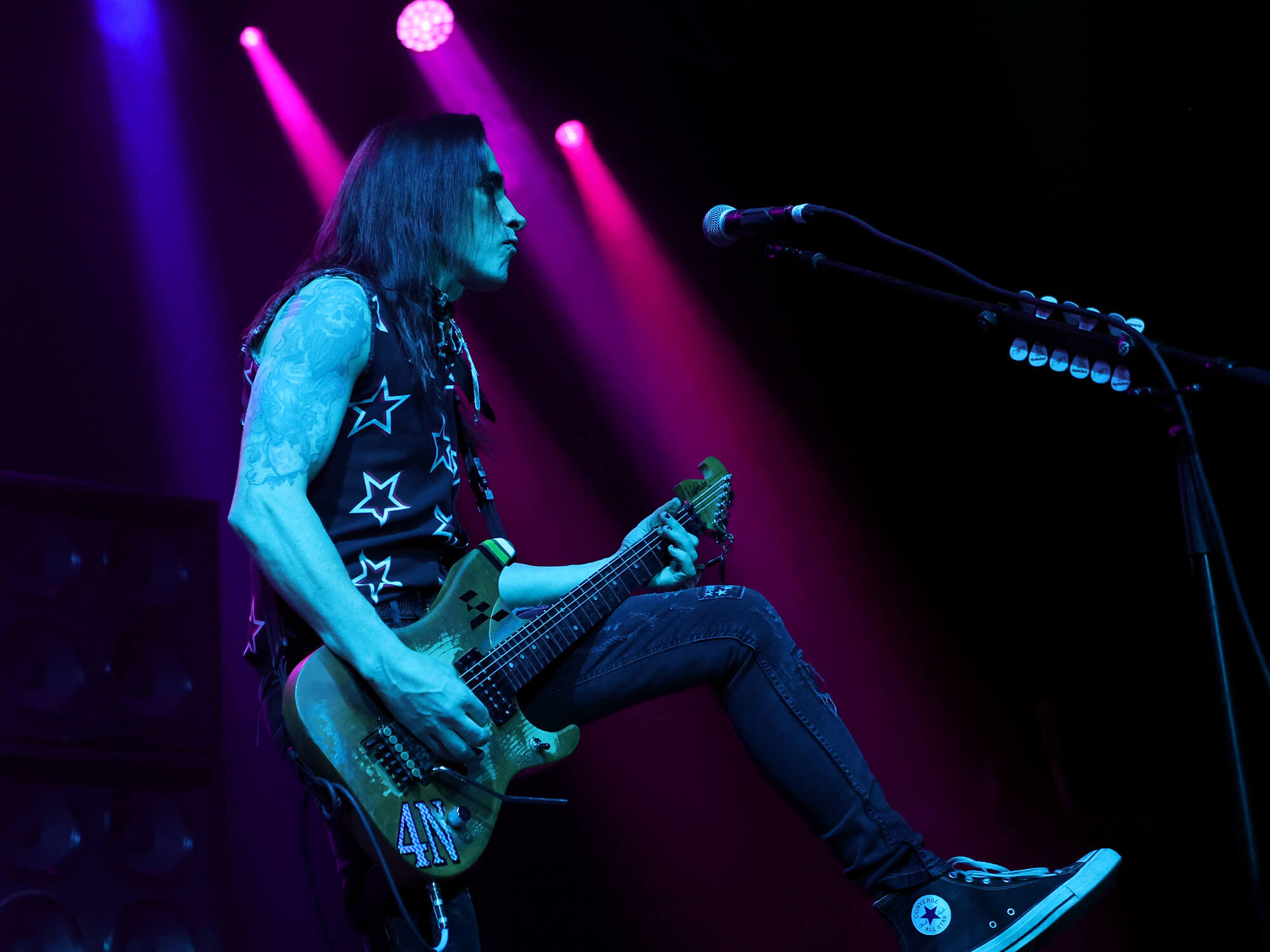 Nuno Bettencourt on stage. He has foot rested on a platform as he is playing guitar.