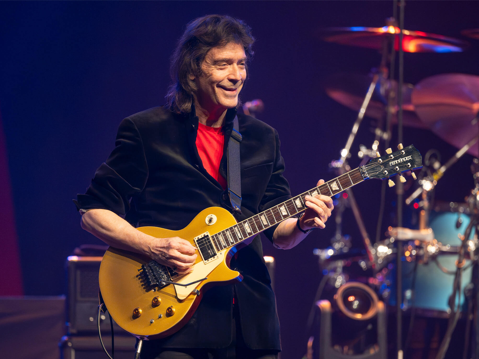 Steve Hackett on stage, pictured smiling as he plays guitar