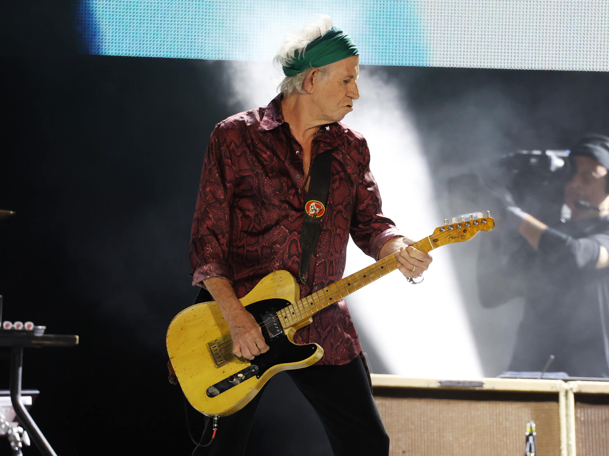 Keith Richards on stage. He has his Telecaster in hand, is wearing a head band and is pulling a pouted, concentrated facial expression.